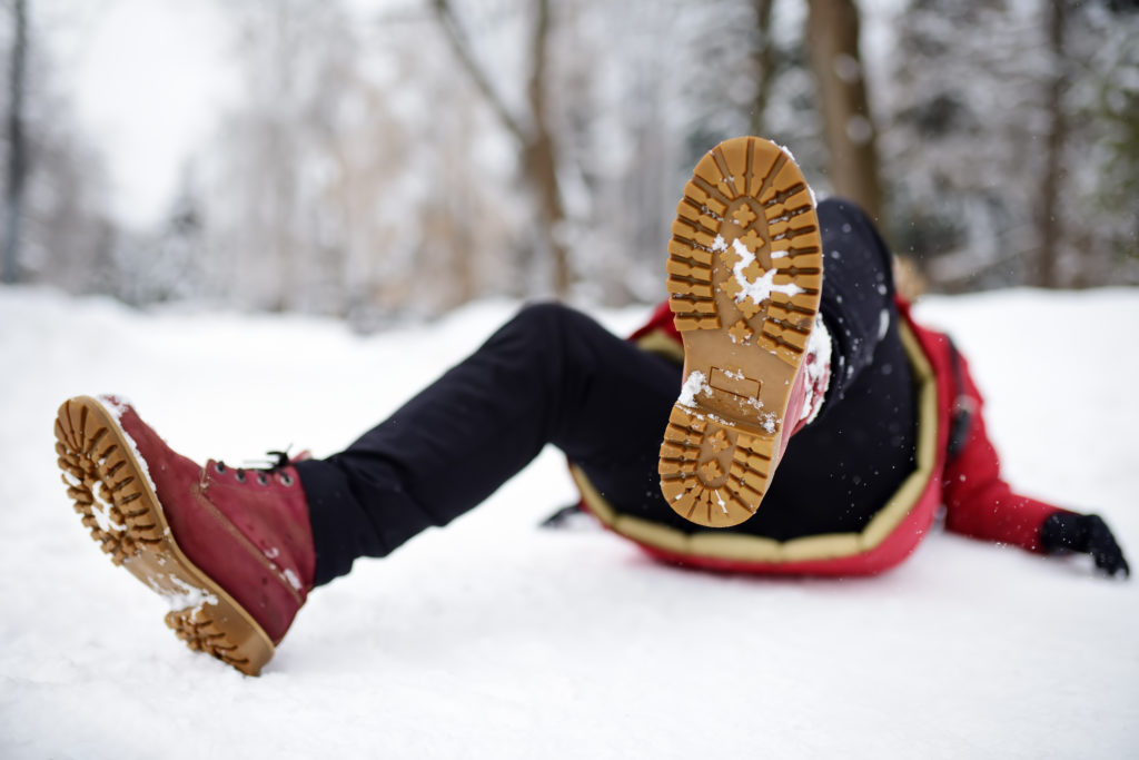 henkilö on kaatunut lumisella tiellä ja makaa niin, että vain jalat ja kengänpohjat näkyvät.